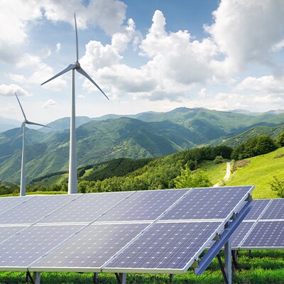 Un paysage montagneux avec au premier plan des moulins à vent et des panneaux solaires.